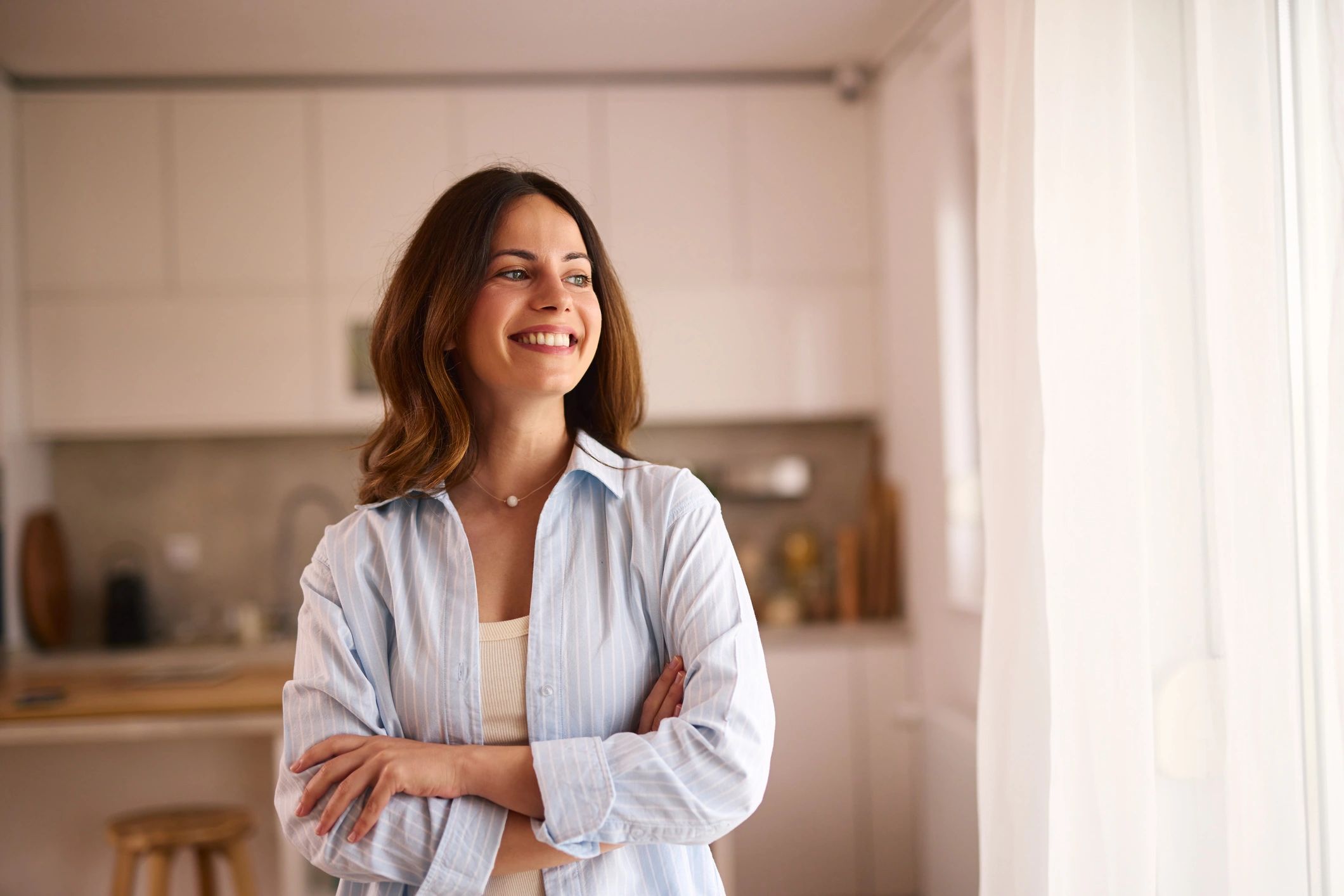 Young Woman Smiling and Looking Away Through the Window in a Modern Kitchen